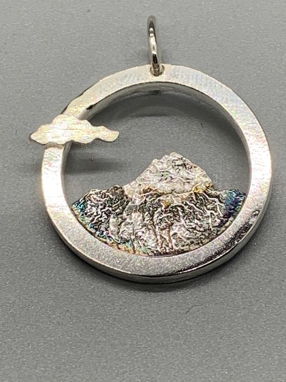 Round pendant with a textured outline of Mount Shasta, oxidized, with a small cloud on the rim.