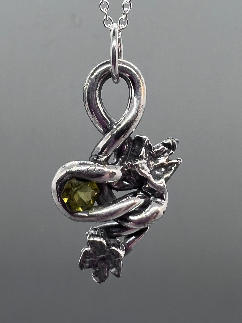 Silver PMC twisted into a vine shape around a six sided green gem with two ivy leaves as embellishments.