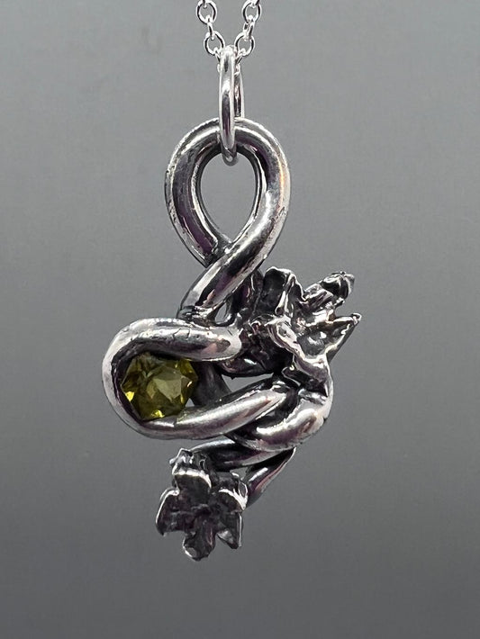 Silver PMC twisted into a vine shape around a six sided green gem with two ivy leaves as embellishments.