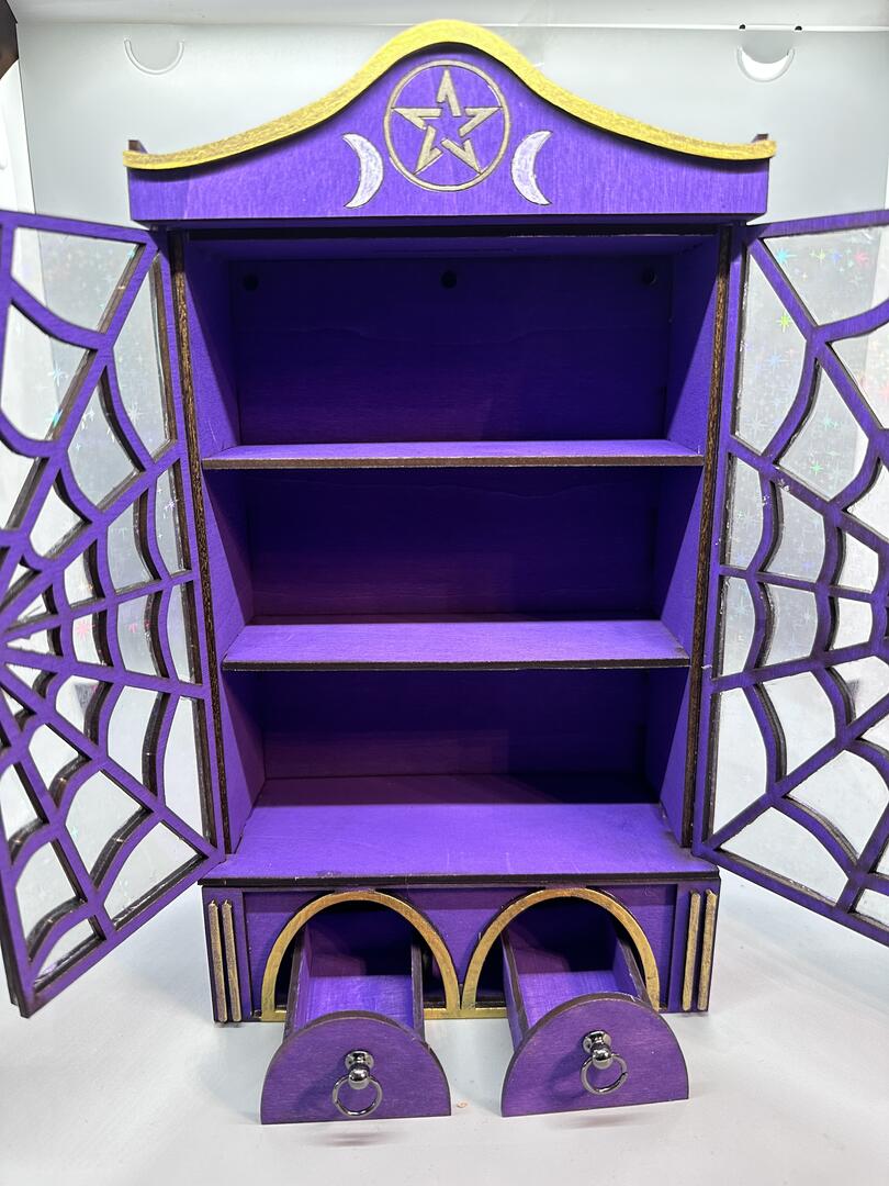 A very purple cabinet/wardrobe with spiderweb doors, open, showeing the two shelves inside and the little drawers at the bottom pulled open.