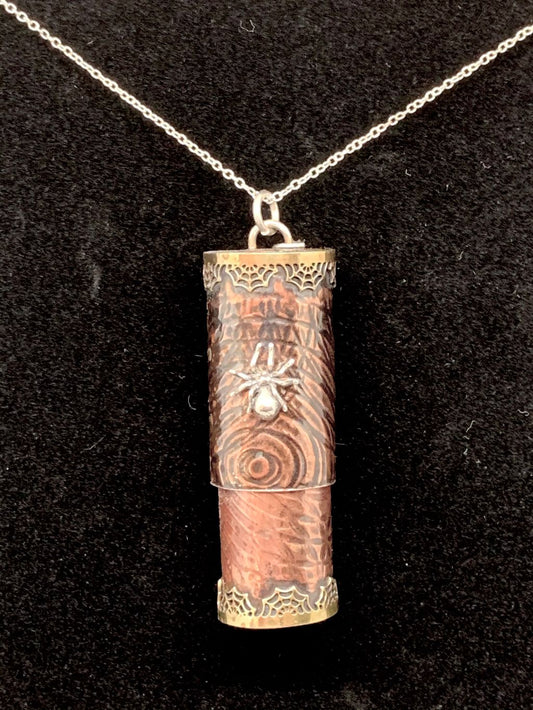 Round copper tube with bayonet closure lid, embellished with circular embossing, a silver spider, and brass spiderweb bezel detail.