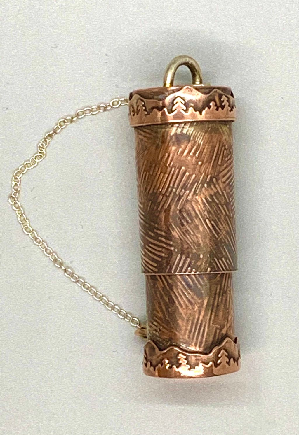 Copper tube with bayonet lock lid patterened with hatchmarks and with a mountain and pine tree bezel.