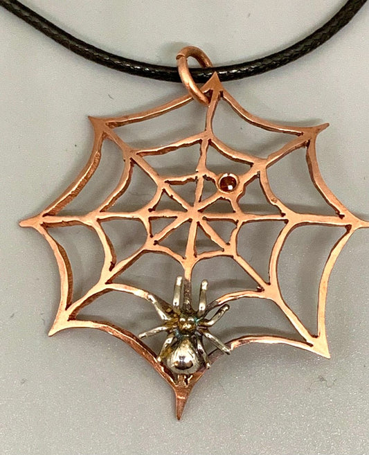 Sawcut copper spiderweb with a garnet stone and a silver spider.