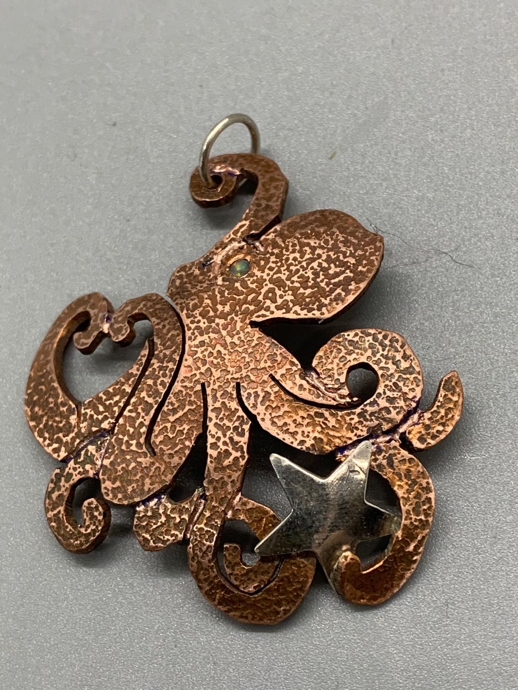 Copper saw-pierced octopus pendant holding a sterling star with an inset opal for an eye.