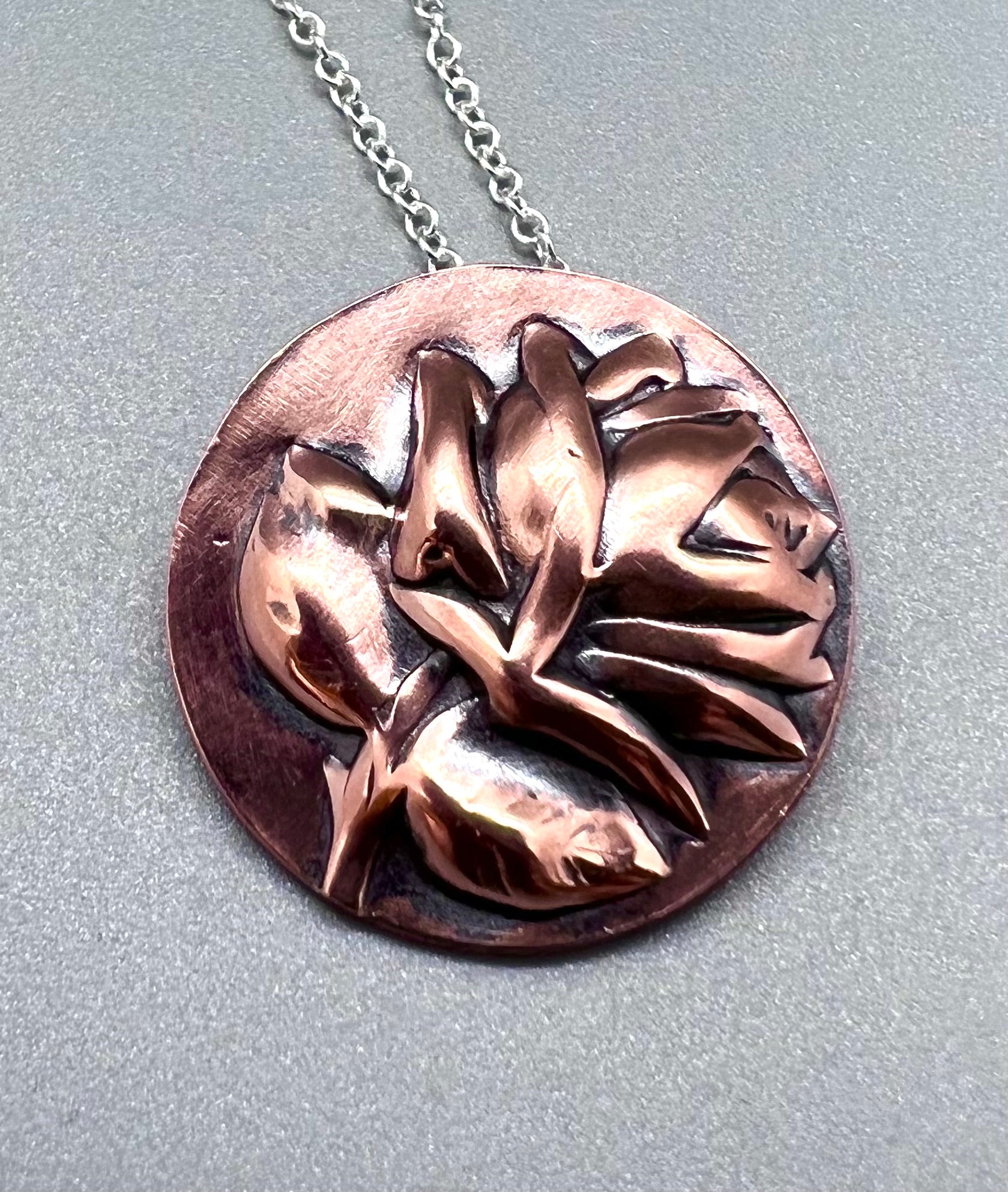 Round copper pendant embossed with a rose and antiqued.