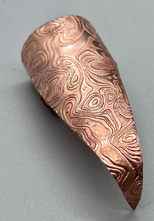 Shiny copper claw embossed with a rorshach-like spilt ink pattern.