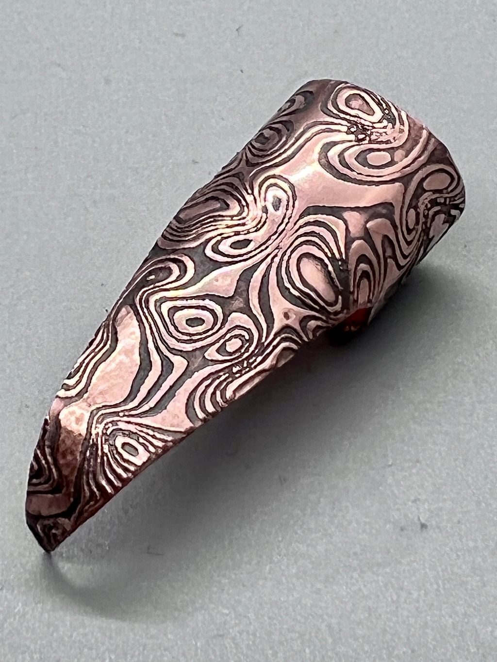 Shiny copper claw embossed with a rorshach-like spilt ink pattern, patina'd and highlighted.