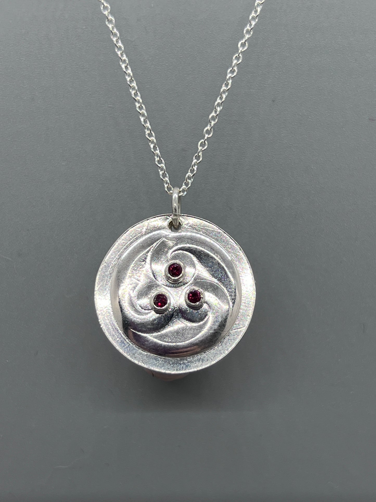 Round silver pendant with three curliques set with three garnets.