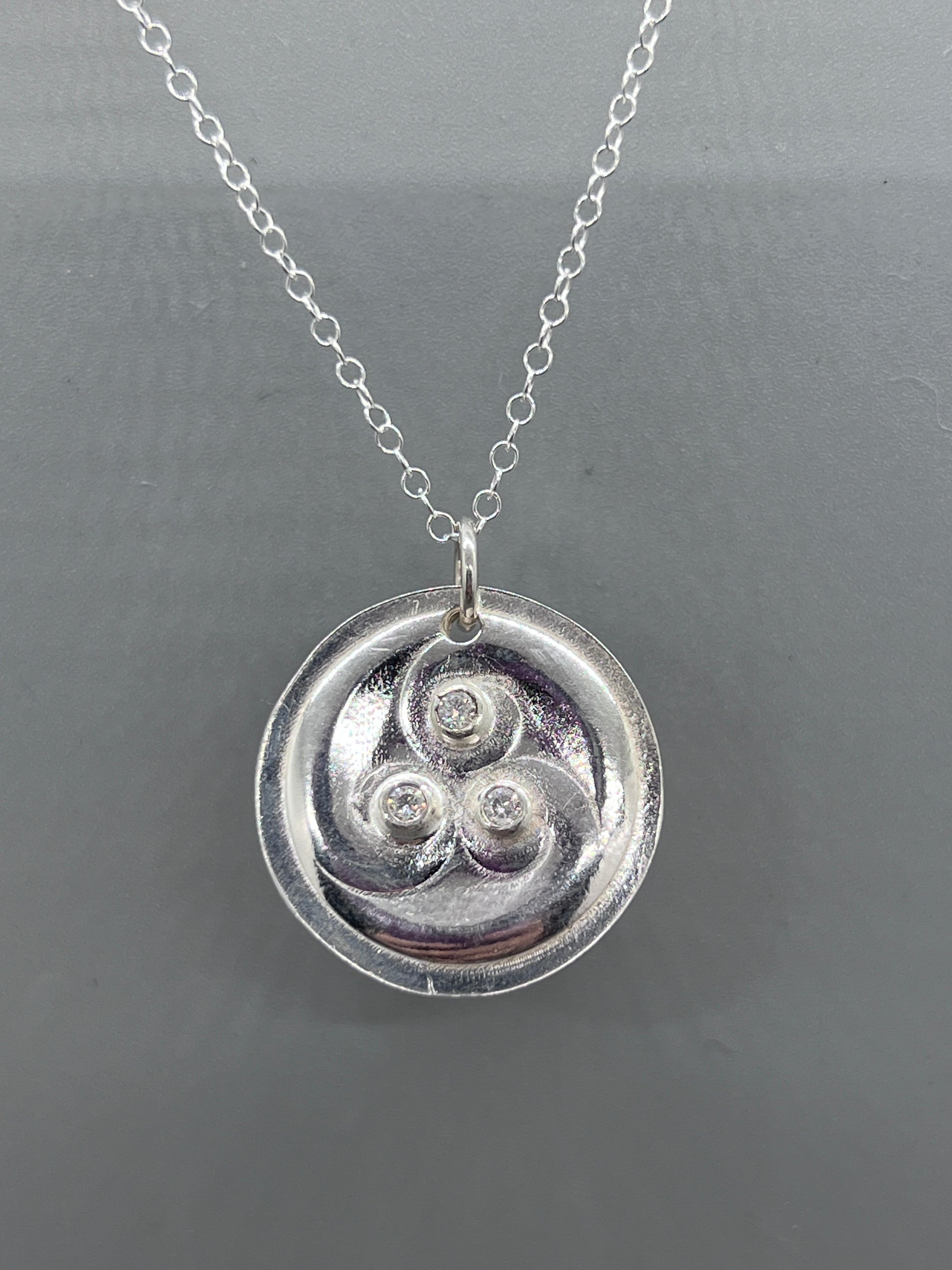 Round silver pendant with three curliques set with three moissanites..