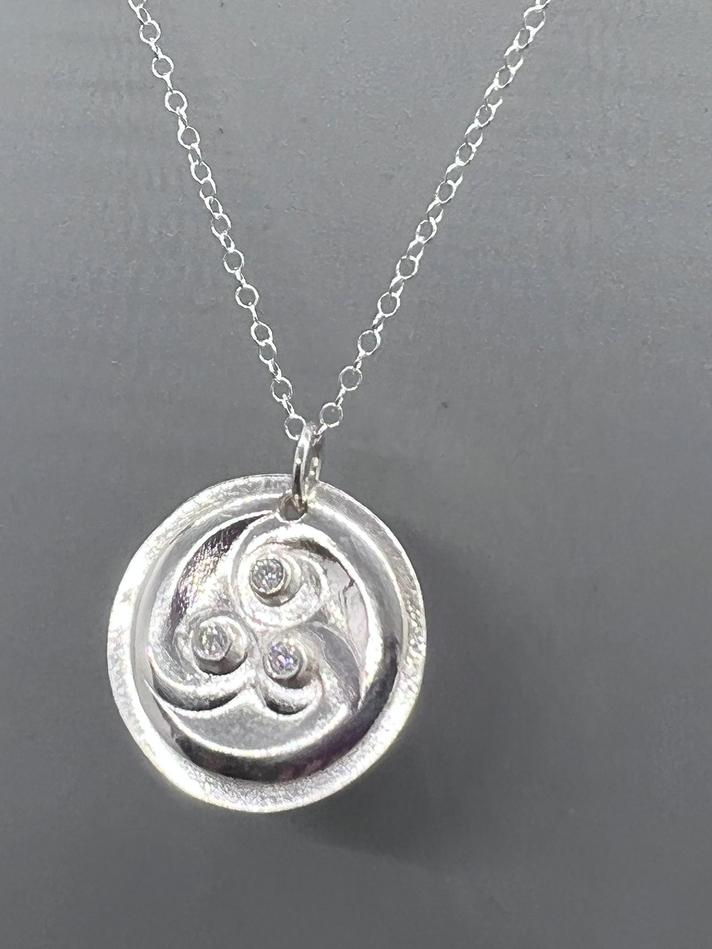 Round silver pendant with three curliques set with three moissanites..