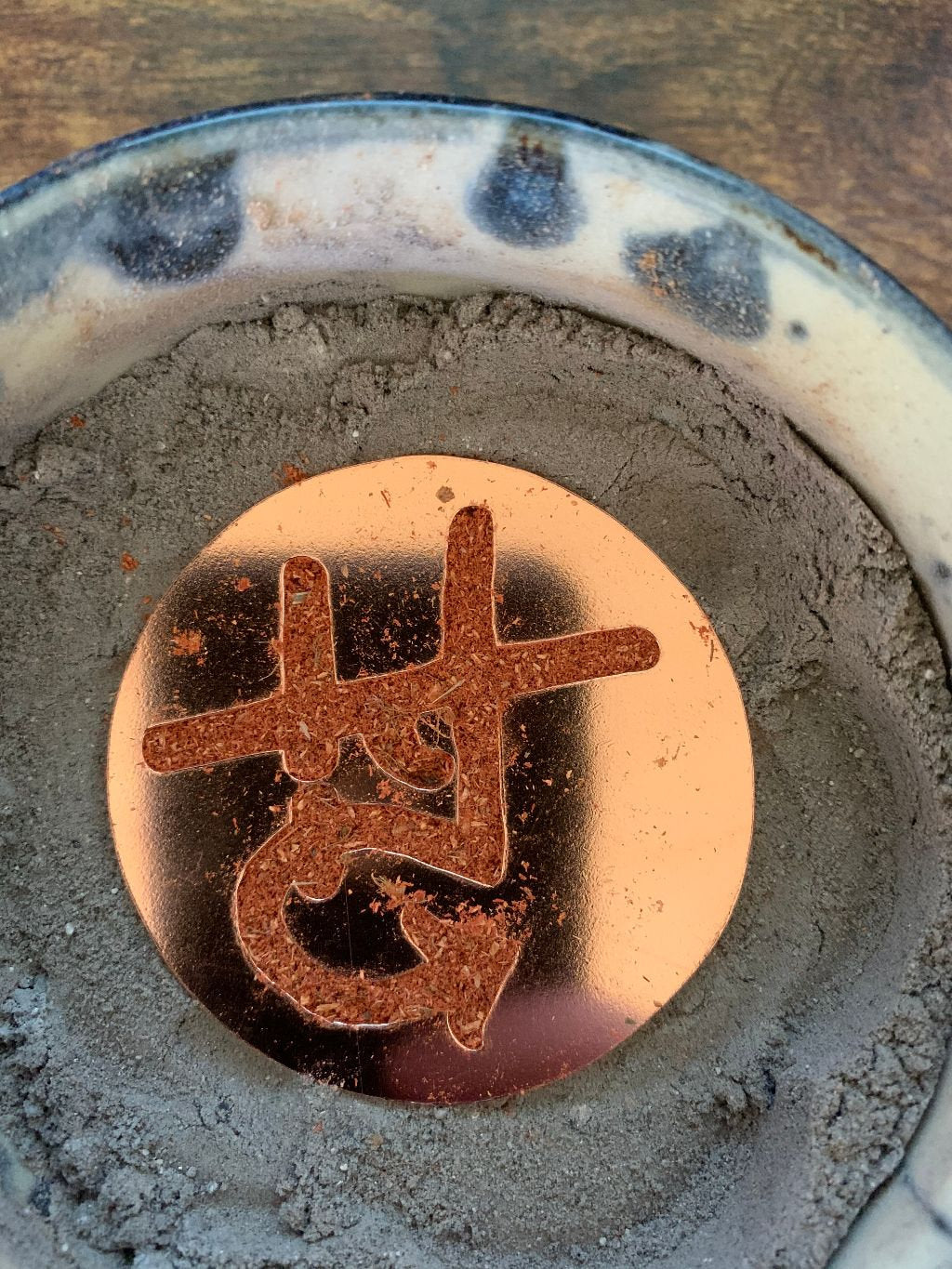 Round copper saw cut logo on ash with incense laid into cut out.